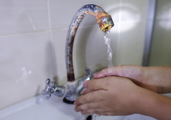 A child washes his hands with water from a rusty tap. Old plumbing, damage and fungus, rust....