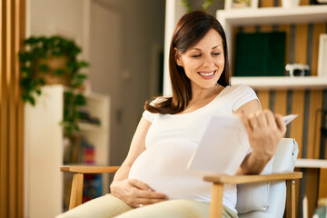 Obraz premium A beautiful smiling pregnant woman, reading a maternity book, sitting at home.
