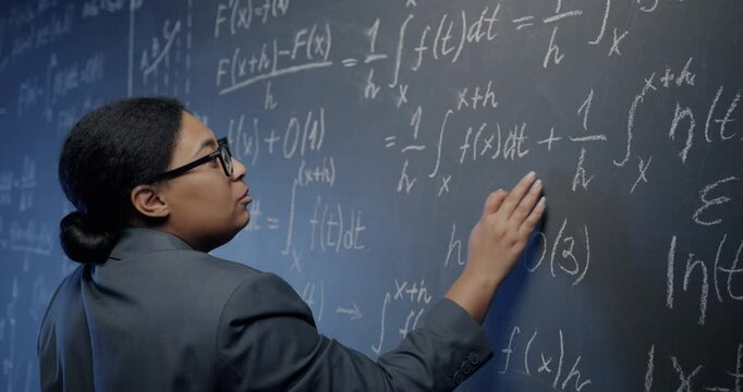 African American woman maths teacher writing on board and speaking explaining formula teaching mathematics in college. Education and knowledge concept.