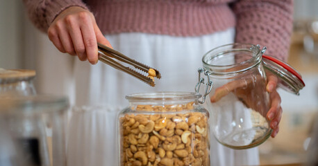 woman hand shopping cashew nuts in glass container with tongs in plastic free shop
