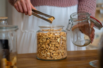cashew nuts taken out of glass bin - woman hand shopping in plastic free store
