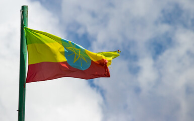 The Ethiopian flag, with its green, yellow, and red stripes and central emblem, waves proudly in the wind against a cloudy sky