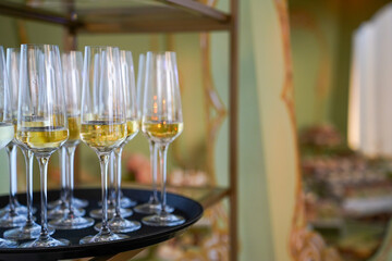 Champagne glasses welcome guests upon entering the restaurant. A waiter is holding a plate with sparkling wine to welcome people at an event. Glasses with champagne to toast.