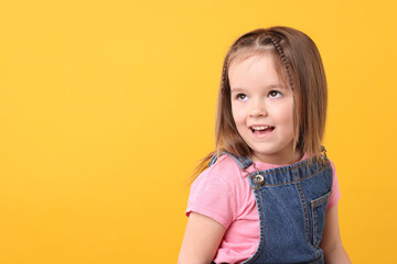 Portrait of cute little girl on orange background, space for text