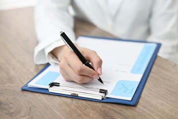Doctor writing prescription at wooden table in clinic, closeup