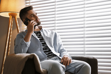 Fototapeta premium Man talking on phone near window blinds at home