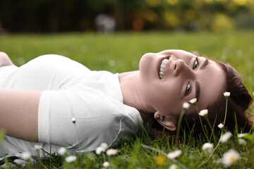 Portrait of smiling woman lying on grass and flowers. Spring vibes