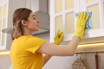 Professional janitor wearing uniform cleaning cabinet in kitchen