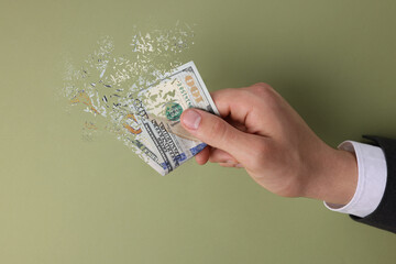 Man holding dissolving dollar banknotes on olive background. Financial crisis