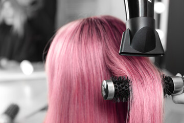 Naklejka premium Hairdresser blow drying client's pink hair in salon, closeup