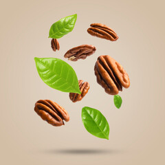 Pecan nuts and green leaves in air on beige background