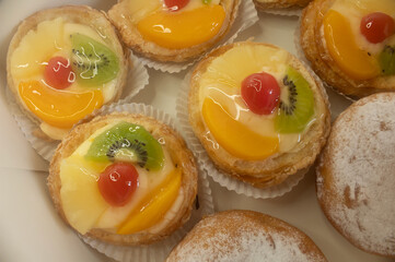 Many danish fruit tartlets and donuts in box.