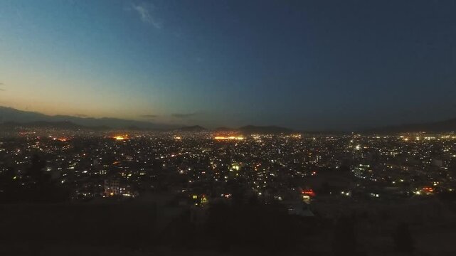 Time lapse panoramic view illuminated Afghanistan capital city Kabul cityscape at night with blue sky and mountain background. Urban landscape panorama at night