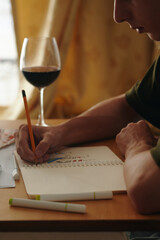 Close-up of designer sitting at table with glass of wine and drawing in album at table