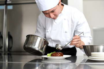 料理を皿に盛る若いアジア人の男性調理師
