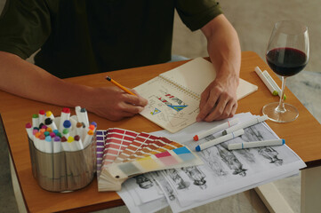 Close-up of designer sitting at his workplace with glass of red wine and working with design...