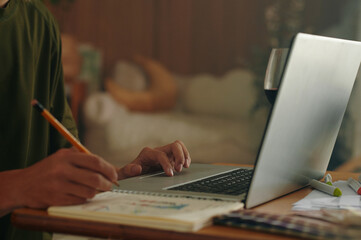 Close-up of designer making notes in album while using laptop at table