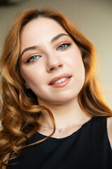 Fototapeta premium Closeup portrait of young curly red-haired elegant woman, with makeup, looking at camera.