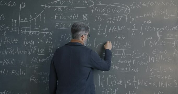 Back view of male scientist writing symbols on chalkboard involved in maths science development in research institute. People and discovery concept.