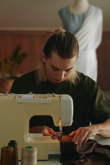 Professional designer sewing fashion collection on sewing machine while working in workshop