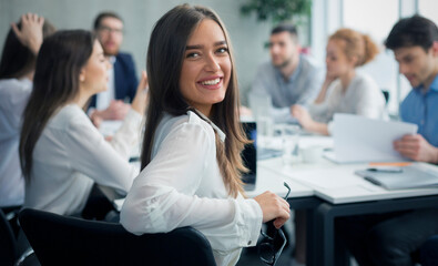 Positive secretary smiling to camera during meeting with colleagues working on background