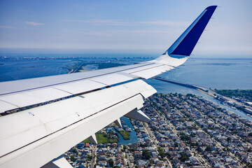 Airplane wing over ocean sea and city landscape in sunny day