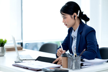 young business woman is writing notes on the data she is viewing on the notebook