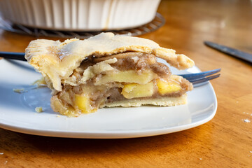 A slice of apple pie sits on a wooden table with a black handled fork.