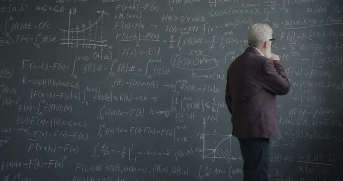 Slow motion of experienced man scientist walking near chalkboard wall thinking about mathematics theory focused on science. People and knowledge concept.
