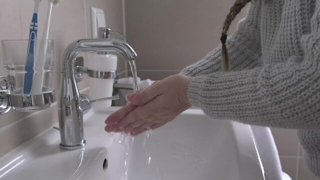 middle-aged woman washing hands in bathroom basin, highlighting importance of good hygiene and self-care for healthy lifestyle