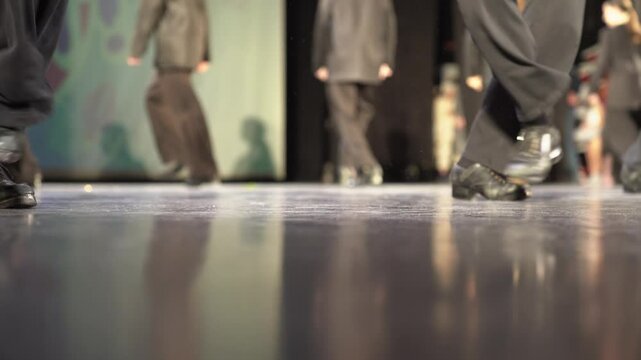 Dancing filmed from below. Women's legs in trousers and black shoes. In stage costumes, they tap dance on a hard floor illuminated by light. A light kick. Selective focus. High quality 4k footage
