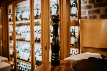 Riga, Latvia March 20, 2024 -  Close-up of a black pepper mill on a wooden table in a cozy restaurant, with a background of wine bottles in wooden cabinets...