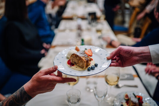 Riga, Latvia March 20, 2024 - A waiter serves a dessert plate with apple strudel, ice cream, and berries at a restaurant, with a blurred background of diners...