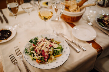 Riga, Latvia March 20, 2024 -  A dinner table setting with a fresh salad, wine glass, and bread basket. Elegant cutlery and glassware are arranged neatly. Copy space.