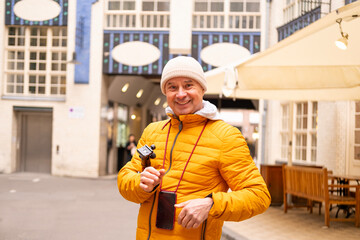 Cheerful middle-aged man, 65 in winter bright yellow puffer jacket and beanie, smiling on urban...