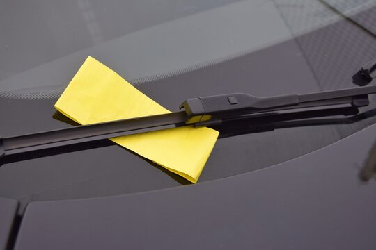 Parking fine notice. A yellow fine ticket under the car wiper.  The vehicle is parked in the wrong place or the parking time has expired.