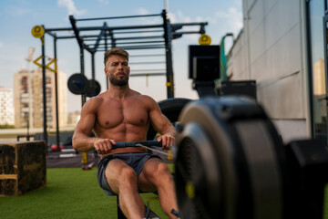 Fototapeta premium A muscular man working out on a rowing machine in an outdoor gym.