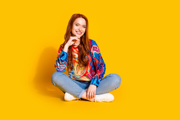 Full length photo of lovely young lady sit floor crossed legs minded dressed stylish colorful garment isolated on orange color background