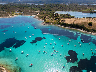 Aerial view of a turquoise lagoon with numerous boats floating on clear water, surrounded by dark...