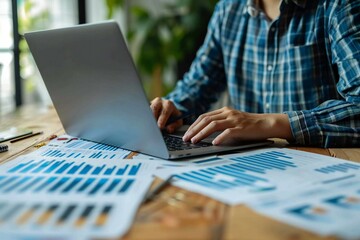 close-up shot of a business analyst or auditor working on statistical data paper documents using a laptop computer with spreadsheets, making analytics reports.
