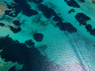 Obraz premium Aerial view of turquoise waters with sunlight reflecting off the surface and dark patches of coral reefs underneath, capturing the serene and natural beauty of the ocean