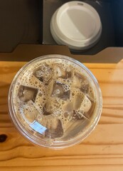 top view of iced coffee in plastic cup next to lids on wood table
