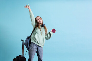 Joyous teenage woman holding passport, going on adventure trip, celebrating arriving at destination. Cheerful wanderlust tourist backpacking, happy to visit attractions, studio backdrop