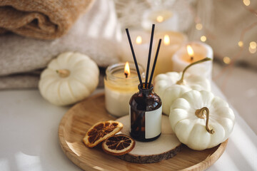 Still life details in the living room. Autumn composition with aroma diffuser with pumpkin pie scent, knitted sweaters, burning candles. Concept of slow life, relaxation, detention. Apartment decor