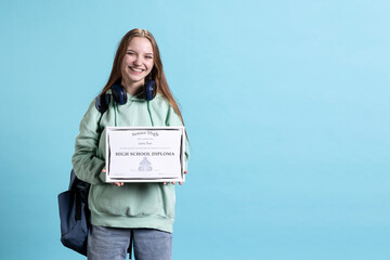 Upbeat young girl holding school award, feeling overjoyed after receiving diploma. Radiant woman smiling after receiving honor, having positive emotion, studio background