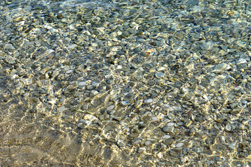 Transparent shallow sea water above pebble beach