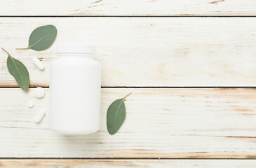 Bottle with pills and green leaves on wooden background, top view