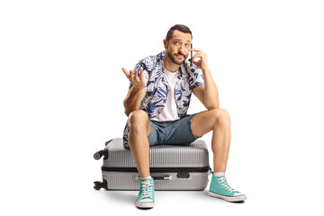 Confused man sitting on a suitcase and using a smartphone