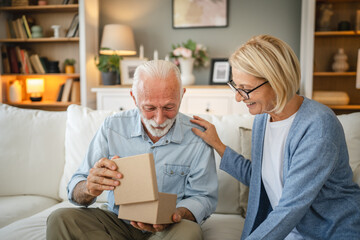 Obraz premium Mature wife surprised her senior husband whit gift while he read book