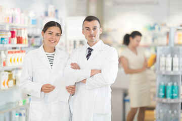 Man and girl pharmacists are standing in pharmacys sales hall, pharmacy staff are amicably preparing to meet chemist shop visitors